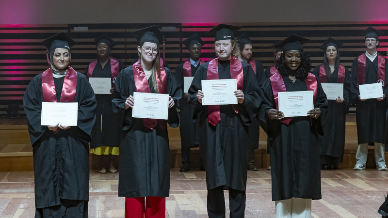 Jeunes diplômés en toge, montrant leur diplôme, sur scène.